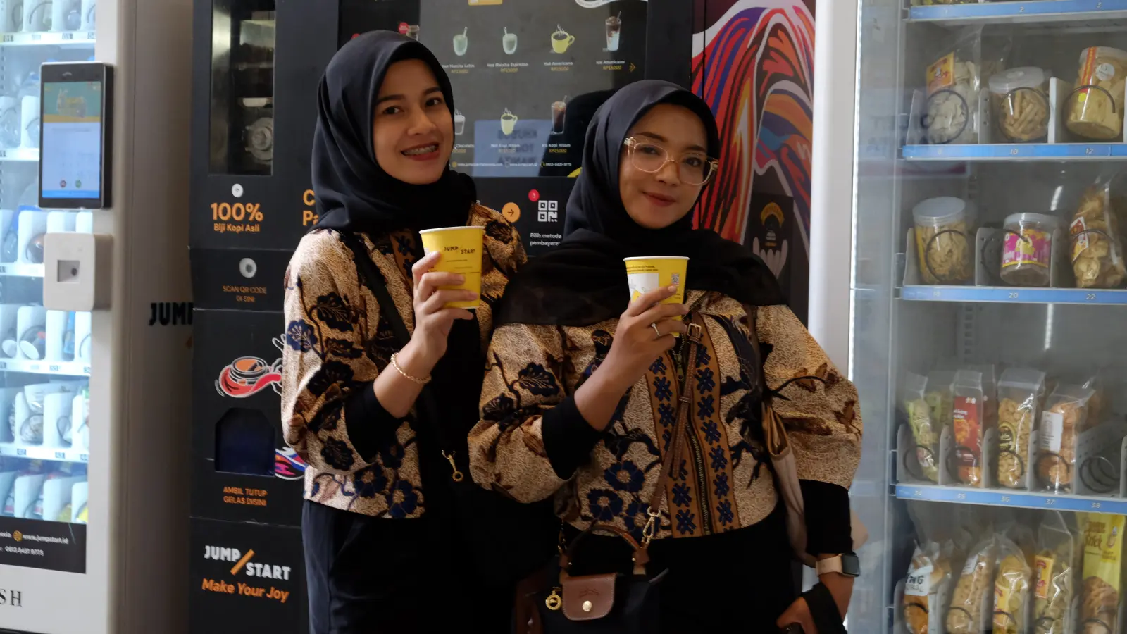 Dua pengunjung memegang kopi dari vending machine JumpStart di Kreasi Bhayangkari Nusantara 2025.