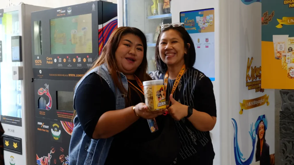 Dua pengunjung memegang camilan dari vending machine JumpStart di acara Kreasi Bhayangkari Nusantara 2025.