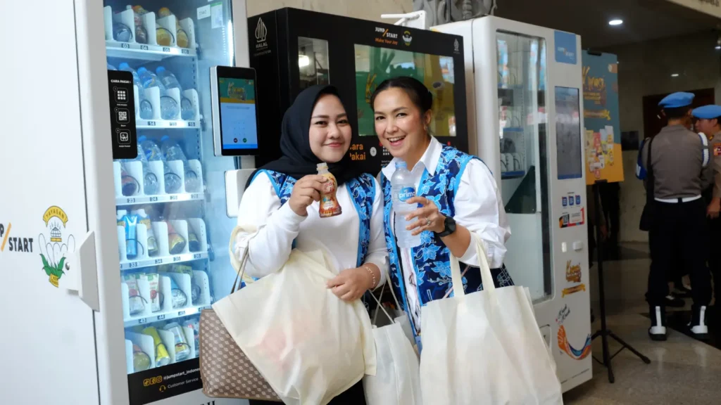 Dua pengunjung memegang minuman botol dari vending machine JumpStart di Kreasi Bhayangkari Nusantara 2025.